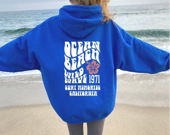 May include: A royal blue hoodie with a white graphic print that says "Ocean Beach Wild Wave 1971 Surf Memories California". The graphic includes a red hibiscus flower.