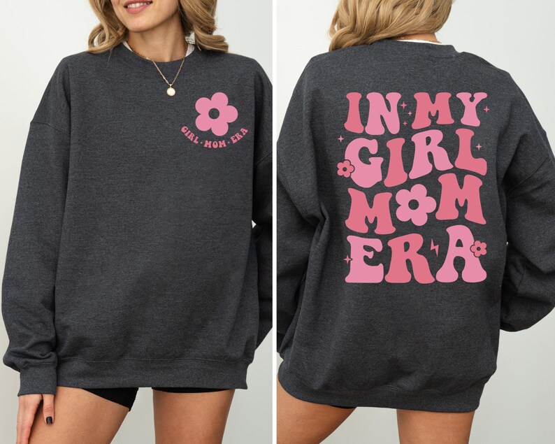 Puede incluir: Sudadera gris oscuro con dise&ntilde;o floral y texto en rosa. La parte delantera presenta una flor rosa y las palabras "GIRL MOM ERA". La parte trasera muestra "IN MY GIRL MOM ERA" en rosa, letras retro.