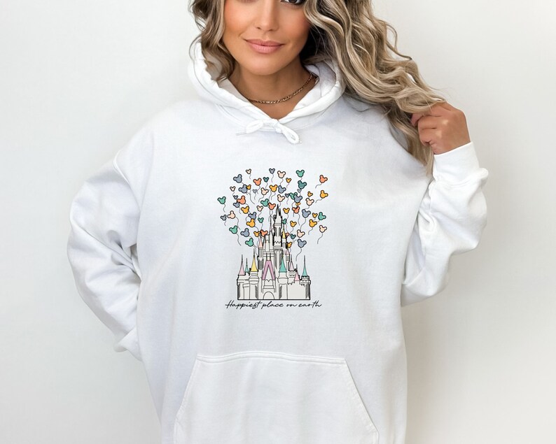 May include: White hoodie with a graphic of Cinderella's castle with colorful Mickey Mouse balloons and the text "Happiest place on earth".