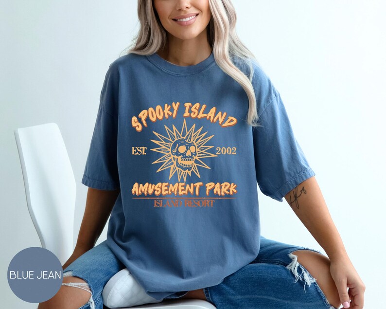 May include: Blue jean t-shirt with the text "Spooky Island Amusement Park" and a skull graphic. The design is in orange and yellow. The shirt is a short-sleeved, casual style.