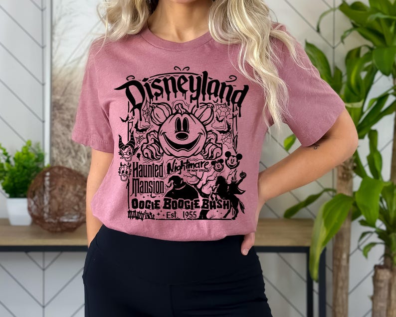 Puede incluir: Camiseta de manga corta color malva con un gr&aacute;fico negro. El gr&aacute;fico incluye la palabra "Disneyland" sobre un dise&ntilde;o de calabaza de Mickey Mouse. El gr&aacute;fico tambi&eacute;n incluye "Haunted Mansion" y "Oogie Boogie Bash".