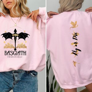 May include: Pink sweatshirt with a black dragon graphic on the front and the text "BASGIATH WAR COLLEGE" and the text "Fly or Die" with gold dragon graphics on the back.