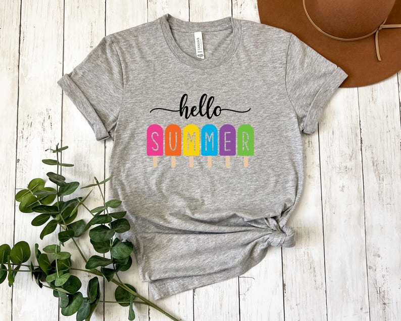 May include: A heather gray t-shirt with the words "hello SUMMER" printed in black script above colorful popsicle graphics. The popsicles are pink, orange, yellow, blue, and green. The shirt is knotted at the waist.