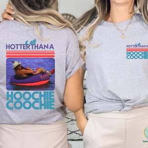 May include: A light gray t-shirt with the text "HOTTER THANA HOOCHIE COOCHIE" in blue and red. The shirt features a graphic of a person in a tube on the water. The same design is on the front and back of the shirt.