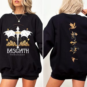 May include: Black sweatshirt with a gold dragon design on the front and a gold dragon design with the text "Fly or Die" on the back. The text "Basgiath War College" is printed below the dragon on the front.