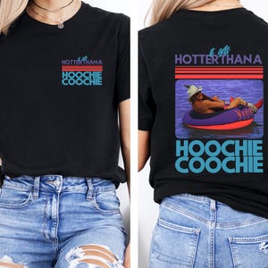 May include: Black t-shirt with the text "HOTTERTHANA HOOCHIE COOCHIE" in purple, red, and blue. The back of the shirt features a graphic of a person in a tube on the water with the same text.