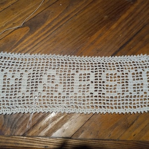 May include: White crocheted doily with a rectangular shape. The doily has a delicate pattern and a scalloped edge.