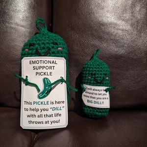May include: Two green crocheted pickle plushies with smiling faces. The larger pickle holds a card that reads "Emotional Support Pickle. This pickle is here to help you "dill" with all that life throws at you!" The smaller pickle holds a card that reads "I will always be around to let you know that you are a big dill!!"