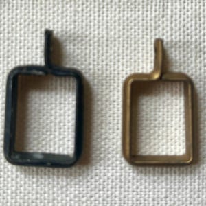 May include: Two rectangular pendant frames with a small loop at the top for attachment. One frame is matte black, and the other is a metallic bronze color. Both frames have a hollow center and a simple, clean-lined geometric shape for jewelry.