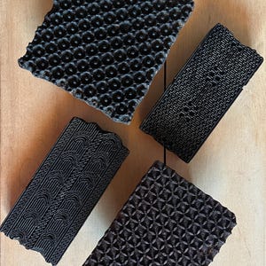 May include: Four wooden printing blocks with different patterns. The blocks are black and have intricate designs carved into them. They are used for printing fabric.