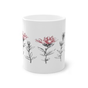 Könnte beinhalten: Weißer Keramikbecher mit floralem Muster. Das Design zeigt rot und schwarz skizzierte Blumen und Blätter. Der Becher ist zylindrisch und hat ein schlichtes Design, für Kaffee oder Tee.