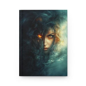 Könnte beinhalten: Hardcover-Journal mit einem Fantasy-Kunstdruck. Das Cover zeigt das Gesicht einer Frau, das teilweise von einem Wolfskopf verdeckt wird, mit leuchtend orangefarbenen Augen und ätherischen blauen und goldenen Akzenten. Das Journal hat einen schwarzen Buchrücken.