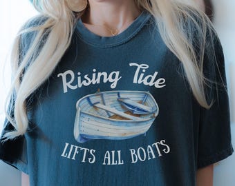 Könnte beinhalten: Ein blaues T-Shirt mit einem weißen Aufdruck eines Bootes und dem Text "Rising Tide Lifts All Boats".
