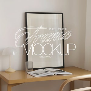 May include: A black picture frame mockup on a desk with a lamp, a glass, and a book. The frame is empty and ready for your design. The text "Photoshop Frame Mockup DIN A Ratio" is visible on the frame.