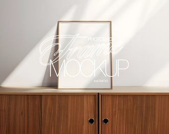 May include: A gold-coloured frame mockup with a 4x5 ratio, sitting on a wooden cabinet with two doors. The frame is empty and has a white background.