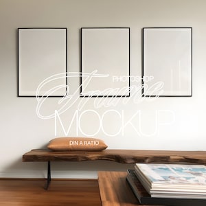 Puede incluir: Tres cuadros enmarcados en negro colgados en una pared blanca sobre un banco de madera con un cojín marrón. El banco está delante de una mesa de café de madera con una pila de libros encima.