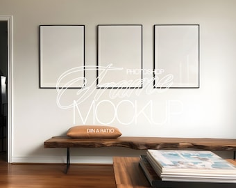May include: Three black framed pictures hanging on a white wall above a wooden bench with a brown cushion. The bench is in front of a wooden coffee table with a stack of books on top.