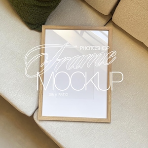 Puede incluir: Un marco de madera con un paspartú blanco y un fondo blanco. El marco está sentado en un sofá beige claro.