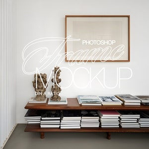 May include: A wooden shelf unit with two shelves, filled with books. A framed picture hangs on the wall above the shelf. The picture has a brown frame and a white background. Two decorative sculptures are on the top shelf.