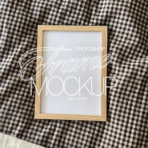 Puede incluir: Un marco de madera con un paspartú blanco y un fondo blanco. El marco está sobre una tela a cuadros blanco y negro.