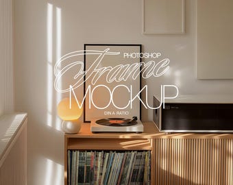 Op de afbeelding: Een zwarte fotolijst mockup met de tekst "PHOTOSHOP FRAME MOCKUP DIN A RATIO" op een witte achtergrond. De lijst staat op een houten plank met een platenspeler en een lamp.