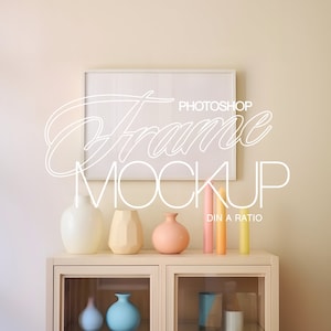 May include: A white picture frame mockup with a white background, hanging on a beige wall. The frame is on a shelf with four colorful ceramic vases and three yellow candles. The text "Photoshop Frame Mockup" is written in white on the wall.