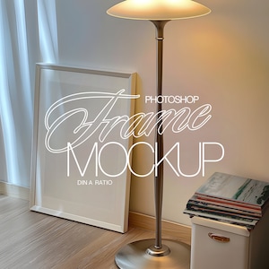 May include: A white picture frame mockup leaning against a wall, with the text "Frame Mockup" in a cursive font. A tall, bronze floor lamp with a round shade stands nearby. A stack of magazines rests on a white storage box.