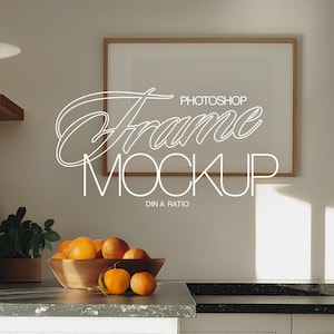May include: A brown wooden frame with a white mat and a white background. The frame is hanging on a white wall above a kitchen counter with a bowl of oranges. The text "PHOTOSHOP Frame MOCKUP DIN A RATIO" is written in white on the frame.