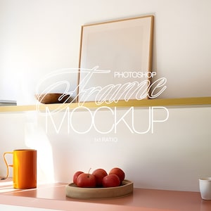 May include: A gold shelf with a wooden bowl, a stack of books, and a framed picture. The shelf is mounted on a white wall. Below the shelf is a pink surface with a yellow mug, a bowl of red apples, and a white mug.