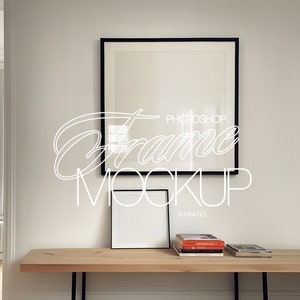 Op de afbeelding: Een zwarte fotolijst mockup met een witte passe-partout en een kleinere zwarte fotolijst mockup op een houten tafel met een stapel boeken. De tekst "PHOTOSHOP FRAME MOCKUP 1x1 RATIO" is zichtbaar op de muur.