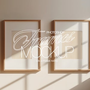 Puede incluir: Dos marcos de fotos de madera con paspartús blancos y fondo blanco. Los marcos están colgados en una pared beige claro. El texto "Photoshop Frames Mockup DIN A Frame Ratio" está escrito en blanco en la pared.