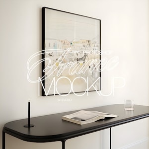 Può includere: Un'immagine incorniciata in nero con un disegno di una scena di città è appesa a una parete bianca sopra un tavolo nero con un libro e un bicchiere d'acqua. Il testo "Frame Mockup 1x1 Ratio" è visibile sotto l'immagine.