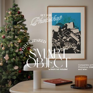 May include: A framed print of a black and white illustration of a pile of scrap metal with the word "RECYCLE" visible. The print is hanging on a white wall next to a Christmas tree decorated with red and gold ornaments. A white lamp and a candle are on a wooden table in the foreground.