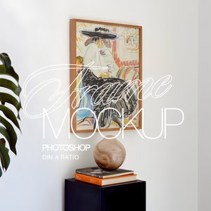 Könnte beinhalten: Ein gerahmtes Kunstwerk mit einer farbenfrohen Skizze einer Person mit Hut. Der Rahmen ist aus Holz. Der Text "Frame Mockup" ist auf dem Bild überlagert. Darunter ein Stapel Bücher und eine dekorative Vase.