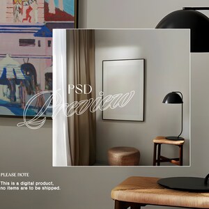 May include: A mock-up of a framed print in a modern interior design setting. The print is white and the frame is black. The room features a brown curtain, a black lamp, and a wooden stool.