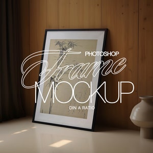 May include: A black framed picture with a black and white image of bamboo plants. The frame is sitting on a light brown surface in front of a wood wall. The text "PHOTOSHOP Frame MOCKUP DIN A RATIO" is written in white on the image.