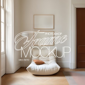 Puede incluir: Un sillón moderno de gran tamaño de color blanco crema con un cojín marrón en una habitación con una gran impresión en lienzo en blanco enmarcada. El texto "Frame Mockup" está escrito en blanco en la pared.