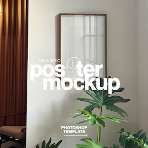 Puede incluir: Una maqueta de póster enmarcado con un marco de madera marrón se muestra en una pared blanca. El texto "DIN A RATIO poster mockup" está superpuesto en la imagen. Una planta verde frondosa está en primer plano y una cortina marrón a la izquierda.