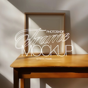 May include: A brown wooden table with a light brown wooden frame sitting on top. The frame is empty and has a white background. The text "PHOTOSHOP Frame MOCKUP 1x1 RATIO FRAME" is written in white on the table.