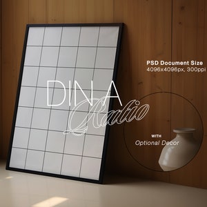 May include: A black framed poster with a white grid pattern and the text "DINA Ratio" in white cursive lettering. The poster is leaning against a wood wall with a white ceramic vase to the right.