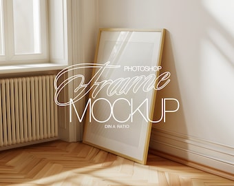 Op de afbeelding: Een gouden fotolijst mockup met een witte passe-partout en een witte achtergrond. De lijst leunt tegen een witte muur met een houten vloer.