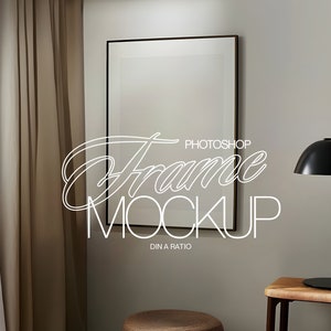 May include: A black framed picture mockup with a white background, hanging on a light beige wall. A brown curtain is to the left of the frame. A black table lamp with a round shade is on the right side of the frame. A small wooden table is below the lamp.