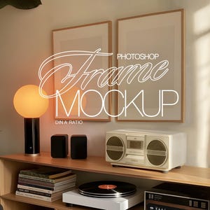 Op de afbeelding: Twee houten fotolijsten met een lichtbruine houten afwerking, de ene boven de andere, op een houten plank. De bovenste lijst is leeg, terwijl de onderste lijst de tekst "PHOTOSHOP" in witte letters heeft. De plank is ook versierd met een lamp, twee luidsprekers en een vintage stereo.
