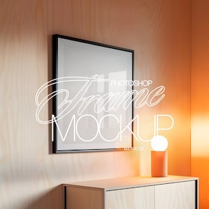 May include: A black picture frame mockup with a white background, hanging on a light wood wall. A small table lamp with a white globe and a peach-coloured base sits on a light wood table.
