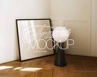 May include: A black frame mockup with a white text overlay that says "Photoshop Frame Mockup 1x1 Ratio Frame". The frame is leaning against a white wall with a white globe lamp in the foreground.