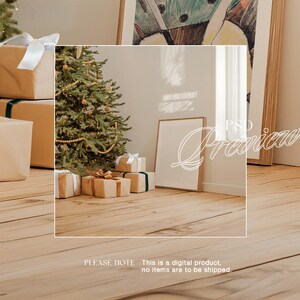May include: A Christmas scene with a decorated Christmas tree, wrapped presents, and a framed picture on a wooden floor. The presents are wrapped in brown paper with white ribbon and gold accents.
