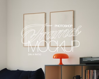 May include: Two wooden picture frames with white mounts hanging on a white wall. The frames are empty and ready for your photos. The frames are in a living room setting with a sofa, a lamp, and a shelf with books and a record player.