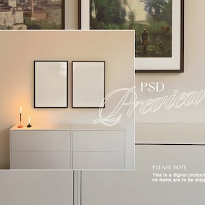 May include: Two black picture frames with white mats hanging on a light beige wall above a white dresser with two drawers. Two candlesticks with lit candles are on the dresser.