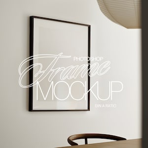 Puede incluir: Una maqueta de marco negro con fondo blanco. El marco está colgado en una pared blanca. El texto "Frame Mockup" está escrito en blanco en el marco. El texto "Photoshop" está escrito en blanco sobre el texto "Frame Mockup". El texto "DIN A Ratio" está escrito en blanco debajo del texto "Frame Mockup".