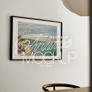 以下が含まれることがあります： ビーチにボートと人々が描かれた海の風景の絵画が額装されています。フレームは黒で、絵画は薄い青、緑、白の色合いです。画像の下には「PHOTOSHOP FRAME MOCKUP DIN A RATIO」というテキストが印刷されています。